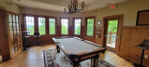 A pool table in a room with large windows, wooden walls, and a chandelier.