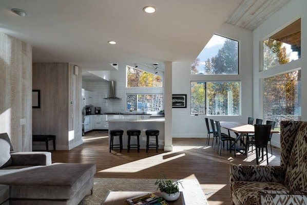 A spacious living area with a large window, a kitchen with a central island, and a dining area with chairs and a table.