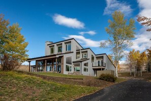 A modern two-story house with a covered patio, large windows, and a stone foundation.