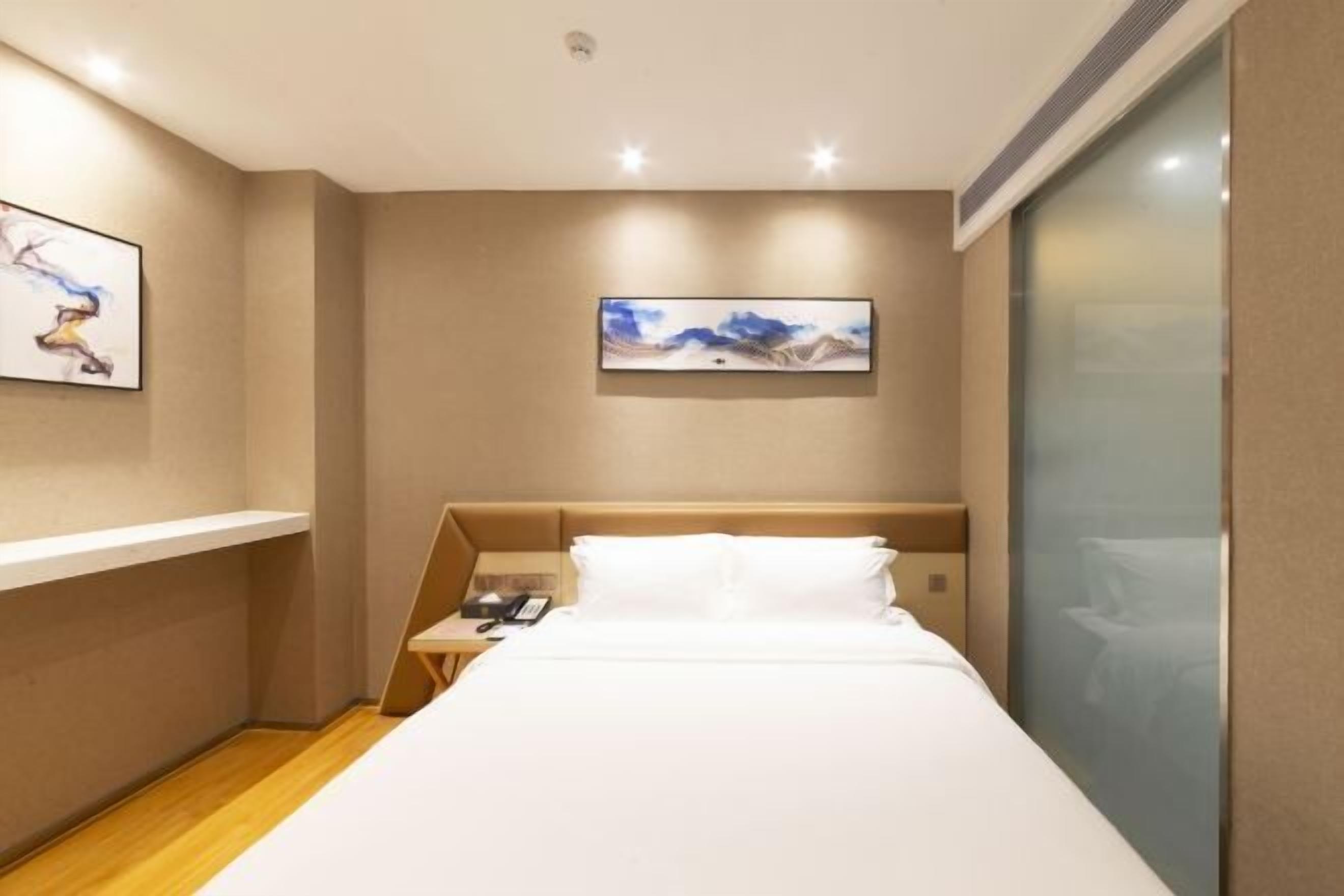 Una habitación de hotel moderna con una cama, una mesita de noche, un cuadro en la pared y una ventana con vidrio esmerilado.