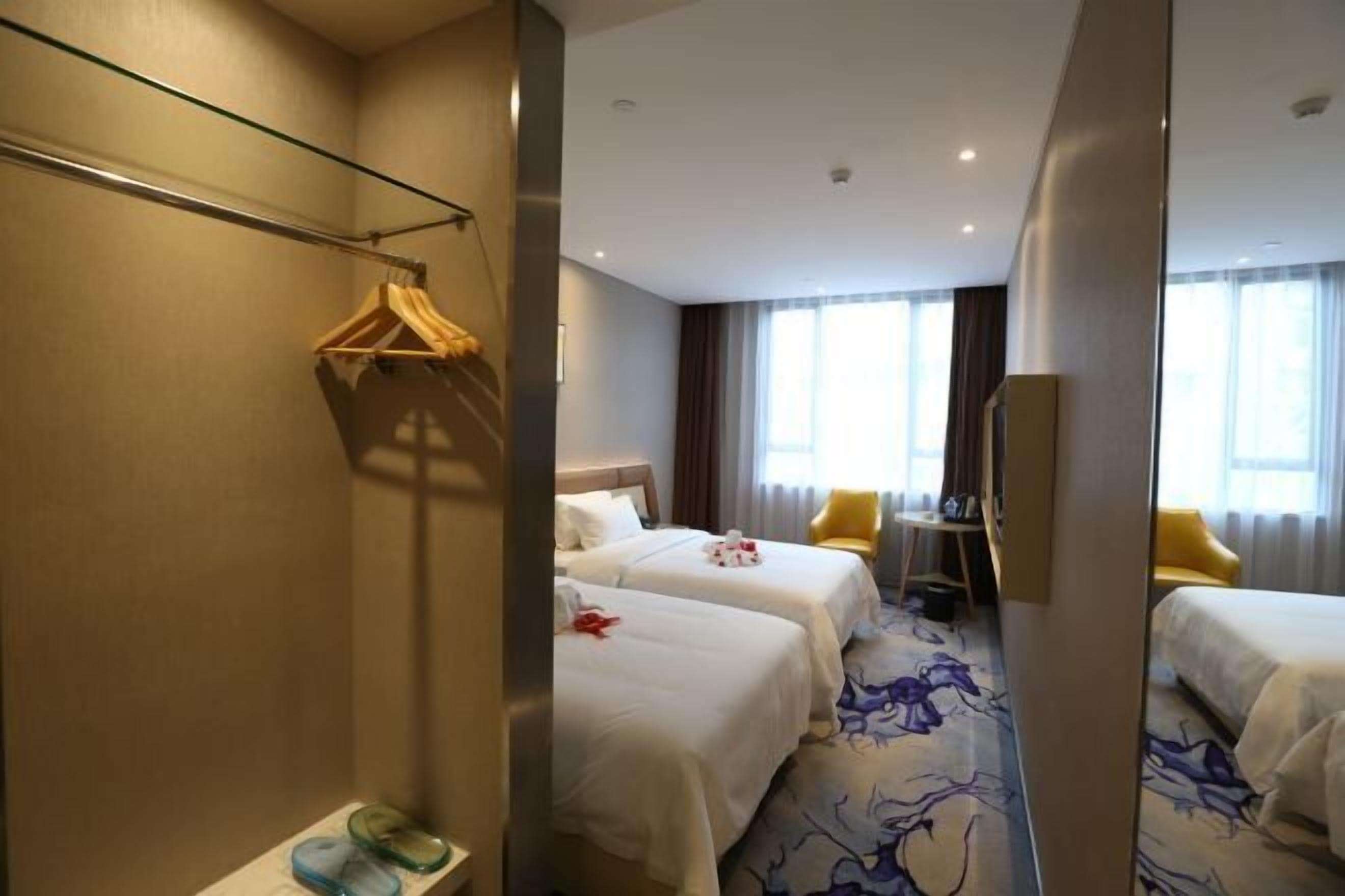A hotel room with two beds, a mirror, a wardrobe, a desk, and a chair.