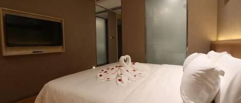 A hotel room with a bed, a flat-screen TV mounted on the wall, and a decorative towel arrangement on the bed.