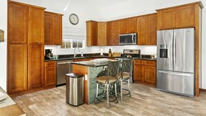 Una cocina moderna con armarios de madera, electrodomésticos de acero inoxidable y una isla central con taburetes de bar.