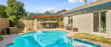 A backyard with a swimming pool, patio furniture, and a covered seating area.