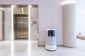A modern elevator with a metallic finish and a digital display, a sleek white pillar, and a white, cylindrical object with a blue light on the floor. - Ji Hotel (Shanghai)