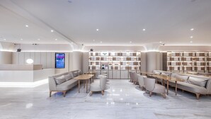A modern hotel lobby with a reception desk, seating areas, and a large bookshelf. - Ji Hotel (Shanghai)