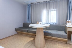 A modern room with a grey sofa, a round wooden table, and a window with sheer curtains. - Ji Hotel (Shanghai)