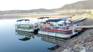 A row of boats docked at a lakeside pier with a calm lake and forested hills in the background. - Aspen Cove resort (Panguitch)