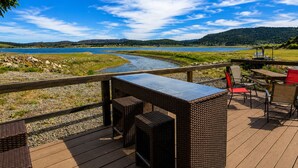 A deck with wicker furniture, a table, and chairs overlooking a river and lake with distant hills. - Aspen Cove resort (Panguitch)
