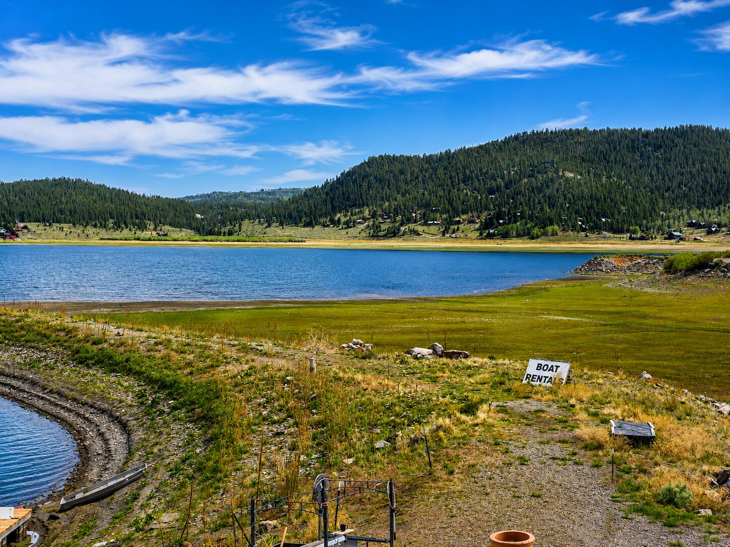 A lakeside view with a boat rental sign, a dock, and a forested hill in the background.
