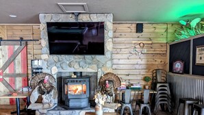 A cozy interior with a stone fireplace, a television mounted above it, and a rustic wooden wall. - Aspen Cove resort (Panguitch)