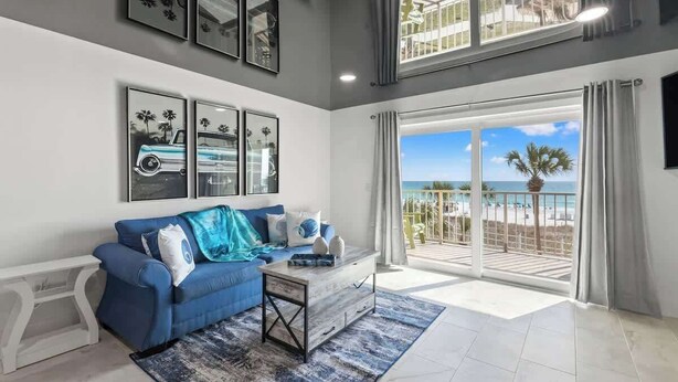 A spacious living room with a blue sofa, a coffee table, and a large window overlooking a beach. - The Summit 306-Beachfront Getaway on the 3rd Floor (Panama City)