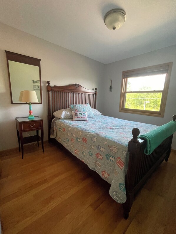 A bedroom with a wooden bed, a bedside table with a lamp, a window with a view, and a wall-mounted mirror. - Waterfront home (Pelican Lake)