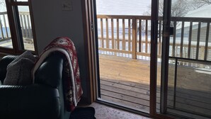 A cozy living room with a view of a wooden deck and a body of water. - Waterfront home (Pelican Lake)