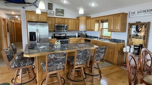 A spacious kitchen with wooden cabinets, a central island with chairs, and a dining table. - Waterfront home (Pelican Lake)