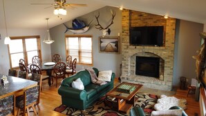 A cozy living room with a fireplace, a dining area with wooden chairs, and a green sofa. - Waterfront home (Pelican Lake)