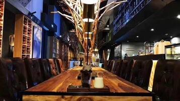 A long wooden dining table with chairs, a modern chandelier, and a bar area in the background.