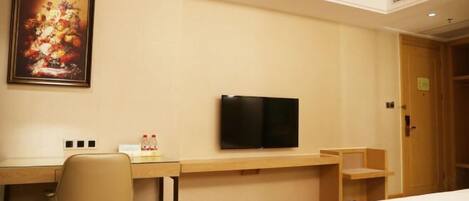 A hotel room with a bed, a desk with a chair, a television, and a painting on the wall.