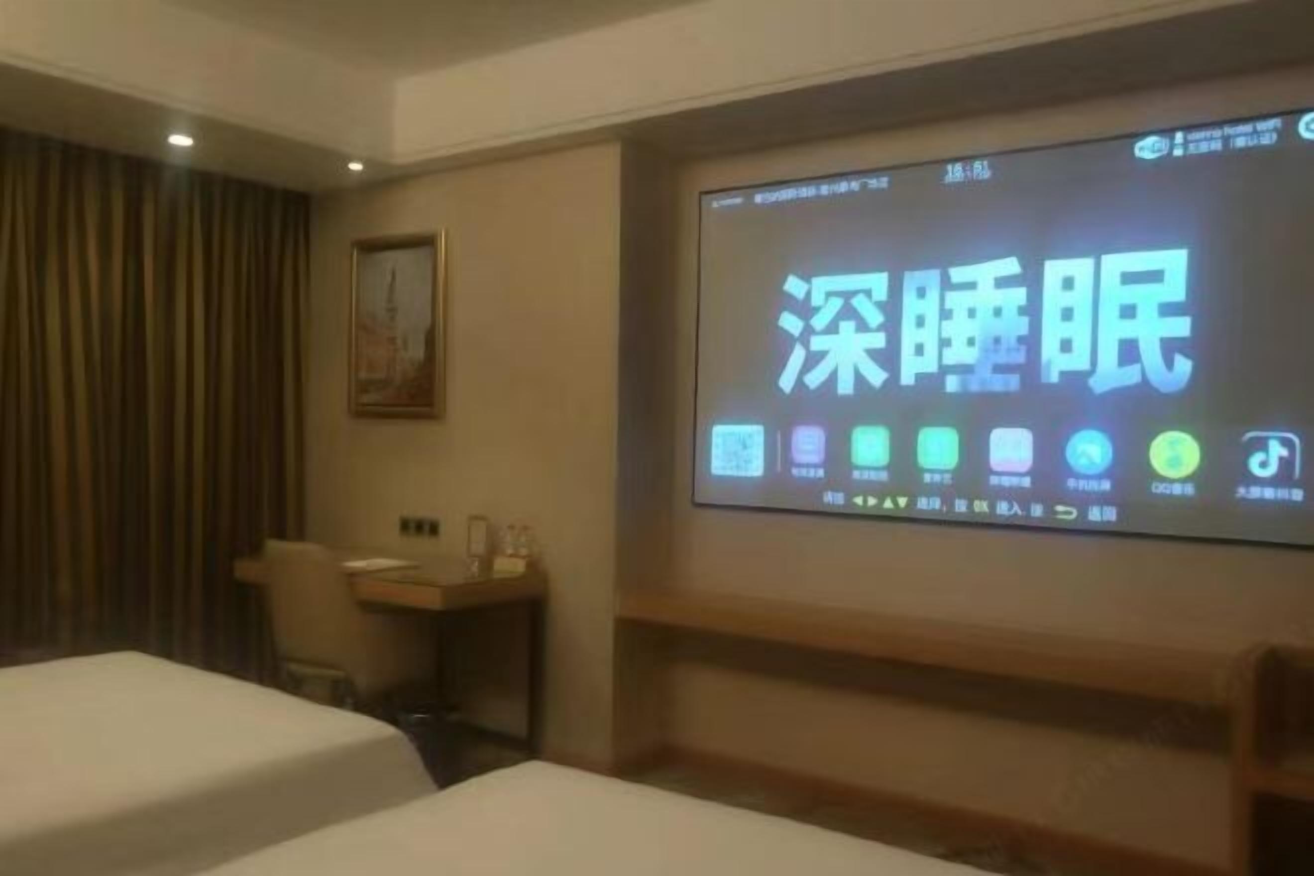 A hotel room with a bed, a desk, and a television displaying Chinese characters.