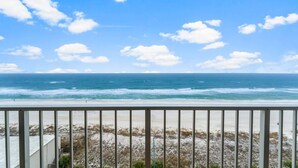 Blick auf einen Strand vom Balkon aus, mit Geländer, Meer und blauem Himmel.