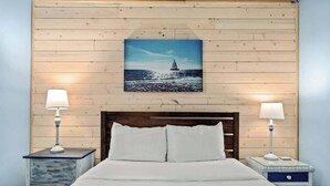 A bed with white linens, two bedside tables with lamps, and a wooden wall with a framed picture of a sailboat. - Sunbird 811E - Beautiful Beachfront Getaway! (Panama City Beach)