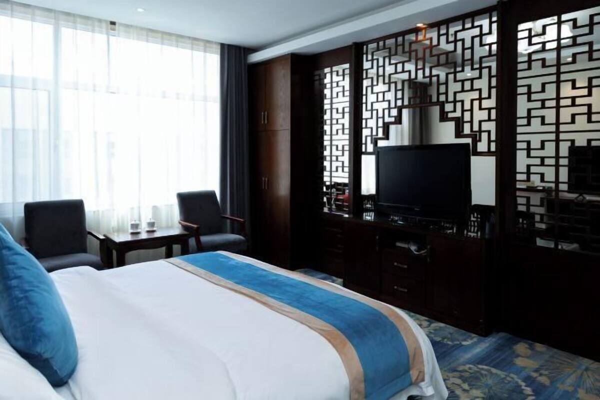 Una habitación de hotel con cama, escritorio, silla, televisor y un biombo decorativo.