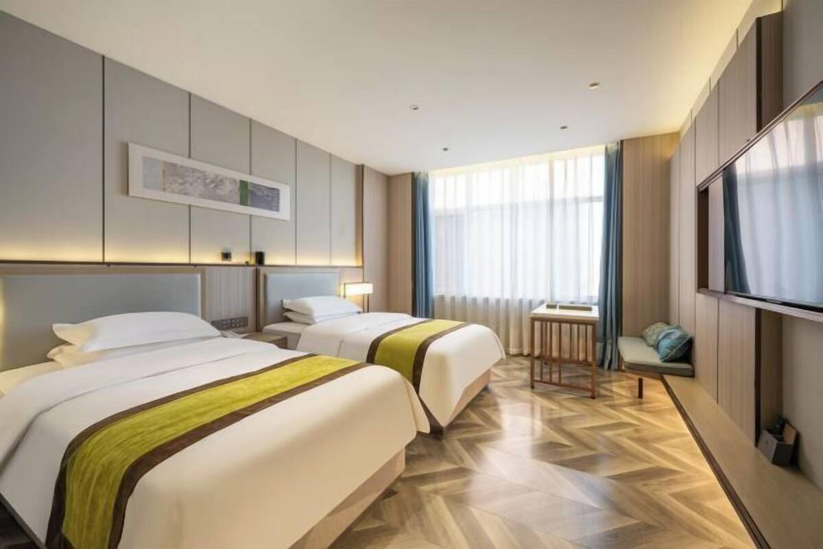 Habitación de hotel con dos camas, un escritorio, una silla, un televisor y una ventana con cortinas.