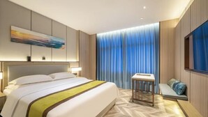 A modern hotel room with a large bed, a bedside table, a small seating area, and a large window with curtains. - Hekou Hotel (Dongying)