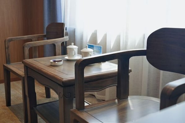 A wooden dining table with chairs, a white teapot, a cup, and a blue card on the table.