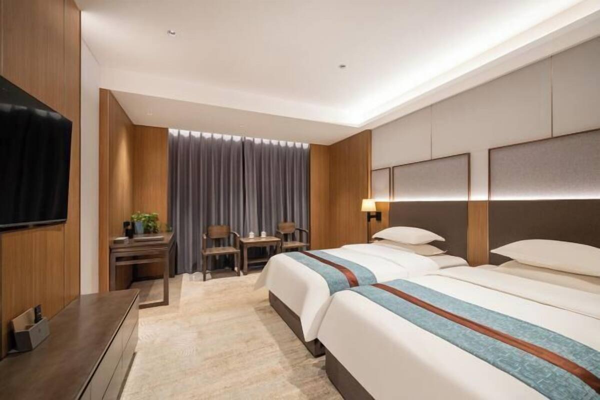 Habitación de hotel con dos camas, un escritorio, un televisor y una zona de estar con cortinas.