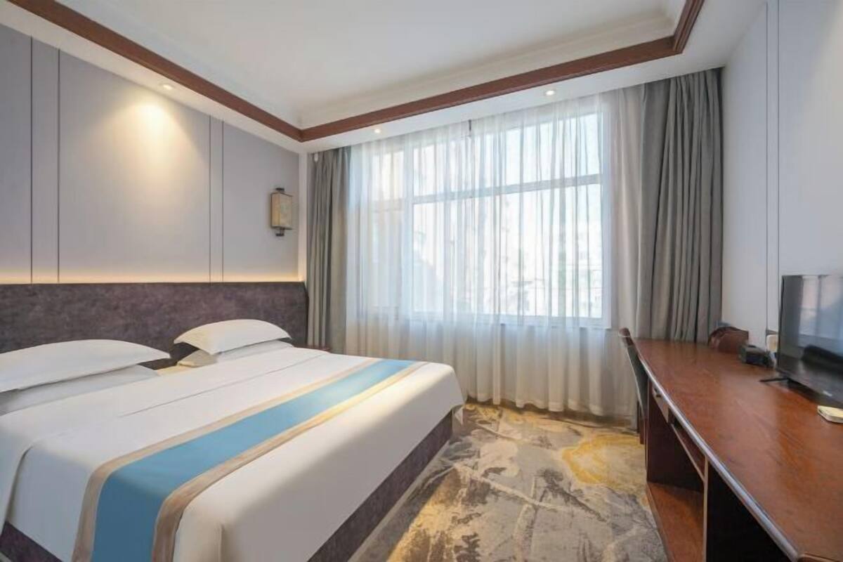 Una habitación de hotel con una cama grande, un escritorio, un televisor y una ventana con cortinas.