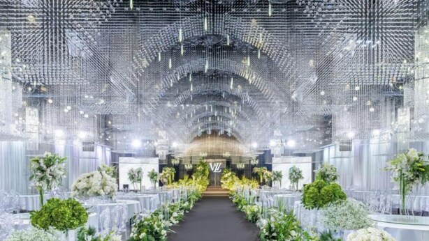 A venue with a central aisle flanked by tables with floral arrangements, a patterned ceiling, and a chandelier. - Hekou Hotel (Dongying)