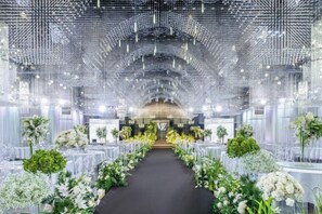 A venue with a central aisle flanked by tables with floral arrangements, a patterned ceiling, and a chandelier.