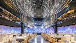 A banquet hall with rows of white tables and chairs, a central aisle, and a ceiling adorned with hanging lights. - Hekou Hotel (Dongying)