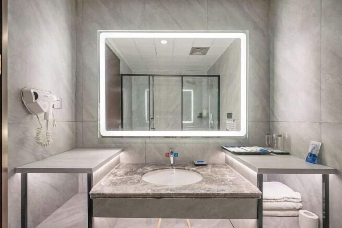 Un baño moderno con un espejo grande, un lavamanos, un secador de pelo y un perchero para toallas.