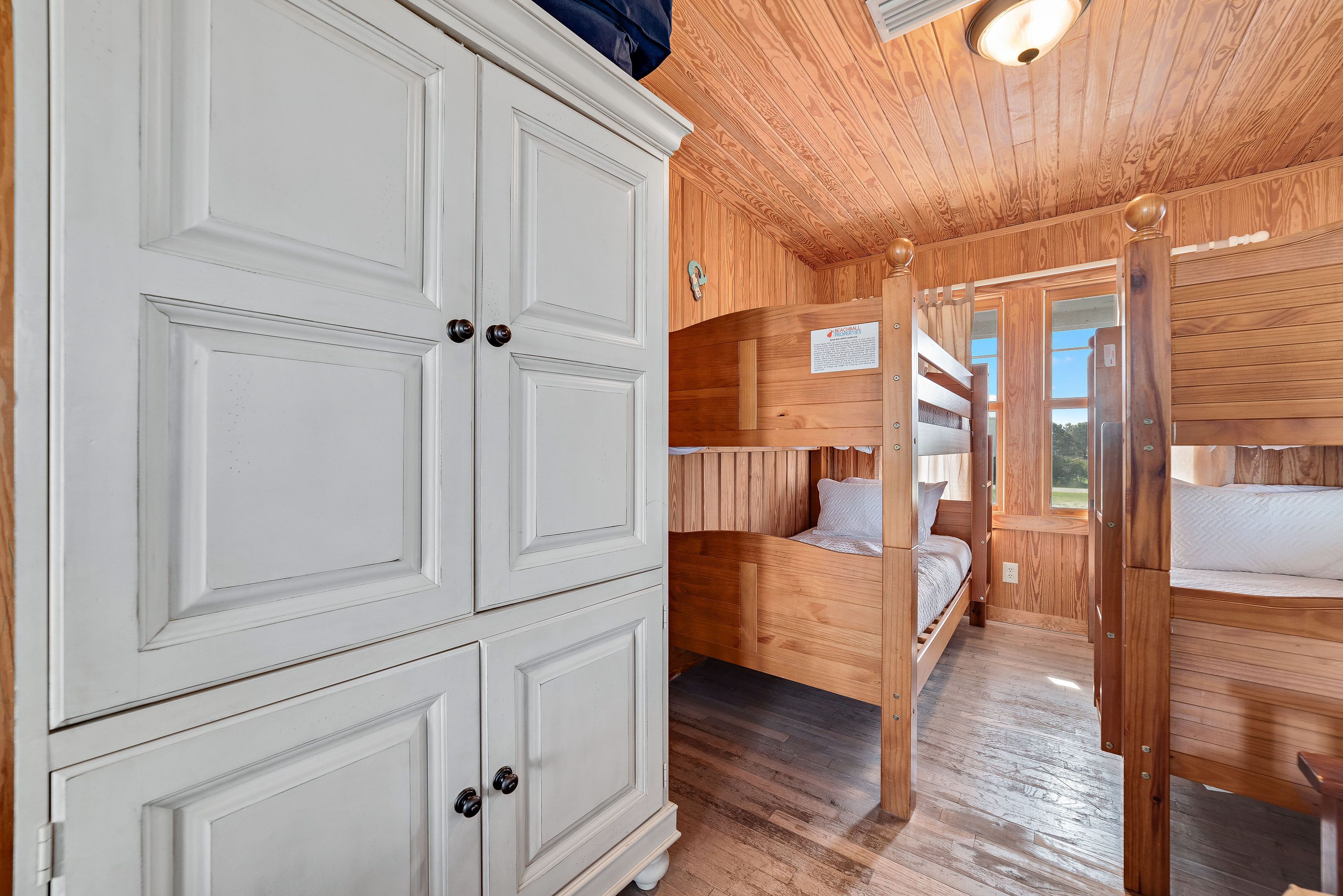 L’intérieur d’un chalet en bois, avec des lits superposés, une armoire blanche et un plafond en bois.