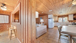 Eine geräumige Küche mit Holzausstattung, ein Essbereich mit großem Tisch und Stühlen und eine Bar mit Hockern.