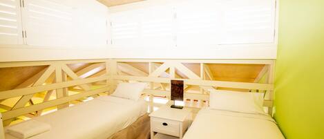 Una habitación con dos camas individuales, una mesita de noche pequeña con lámpara y estructura de techo de madera.