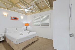 A bedroom with a bed, a nightstand, a lamp, a ceiling fan, a window with blinds, and a door.