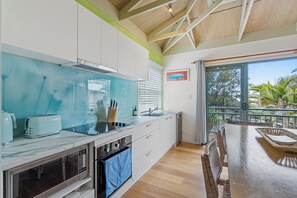 A modern kitchen with a large window, a dining area with a view, and a balcony with a railing.