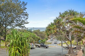 A coastal road with parked vehicles, lush greenery, and a view of the ocean.
