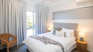 A bedroom with a bed, a chair, a ceiling fan, and a window with curtains. - The Lookout Beach House - Gorgeous renovated 2 level home with spectacular ocean views (Point Lookout)