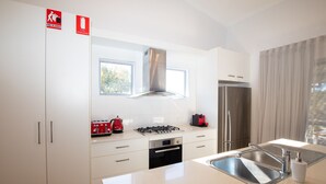 A modern kitchen with white cabinets, stainless steel appliances, a gas stove, and a built-in oven. There are two windows providing natural light, and a stainless steel refrigerator is visible. - The Lookout Beach House - Gorgeous renovated 2 level home with spectacular ocean views (Point Lookout)