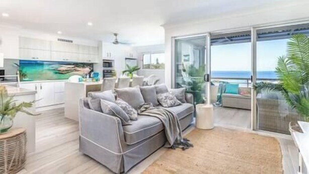 A modern living room with a grey sofa, a flat-screen TV, and a large window offering a view of the ocean. - The Cove - Jewel by the Sea (Point Lookout)
