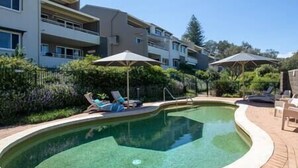 A swimming pool with lounge chairs and umbrellas, surrounded by a brick patio and greenery. - The Cove - Jewel by the Sea (Point Lookout)