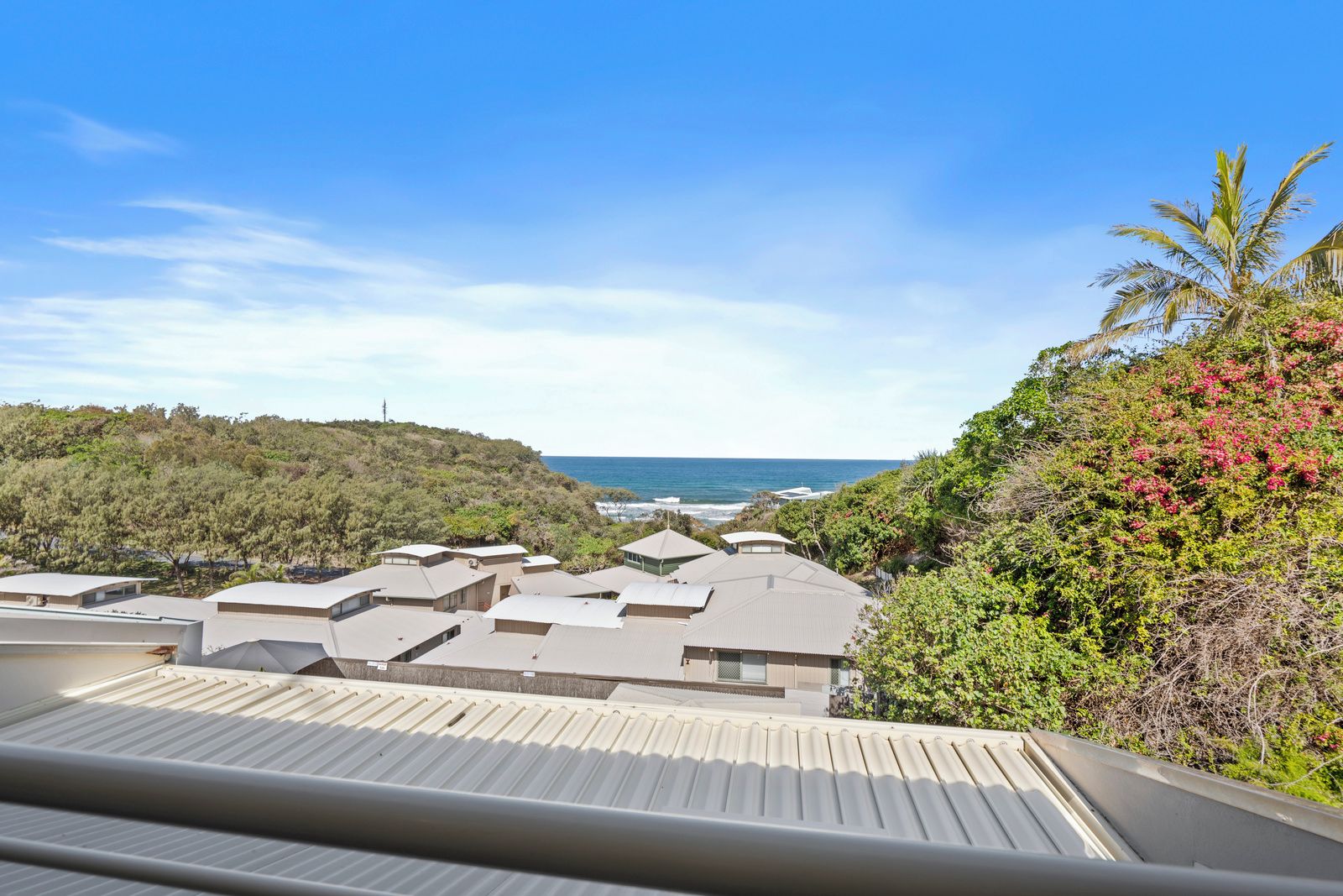 A coastal residential area with multiple houses, a clear sky, and a view of the ocean.