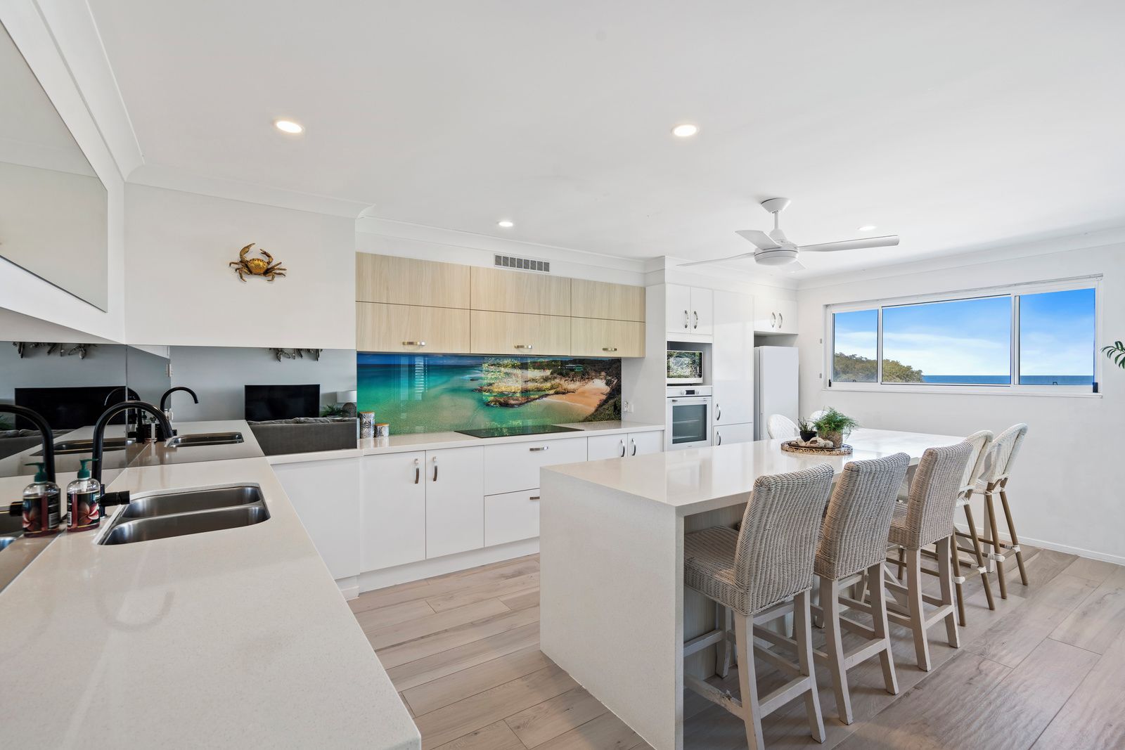 A modern kitchen with a central island, white cabinetry, and a large window overlooking the sea.