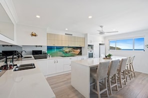 Een moderne keuken met een centraal eiland, witte kasten en een groot raam met uitzicht op zee.