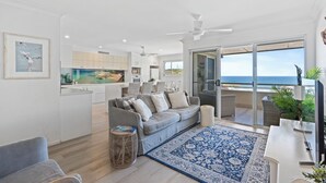Una sala de estar moderna con un sofá gris, un tapete estampado azul y vista al mar a través de un ventanal corredero.