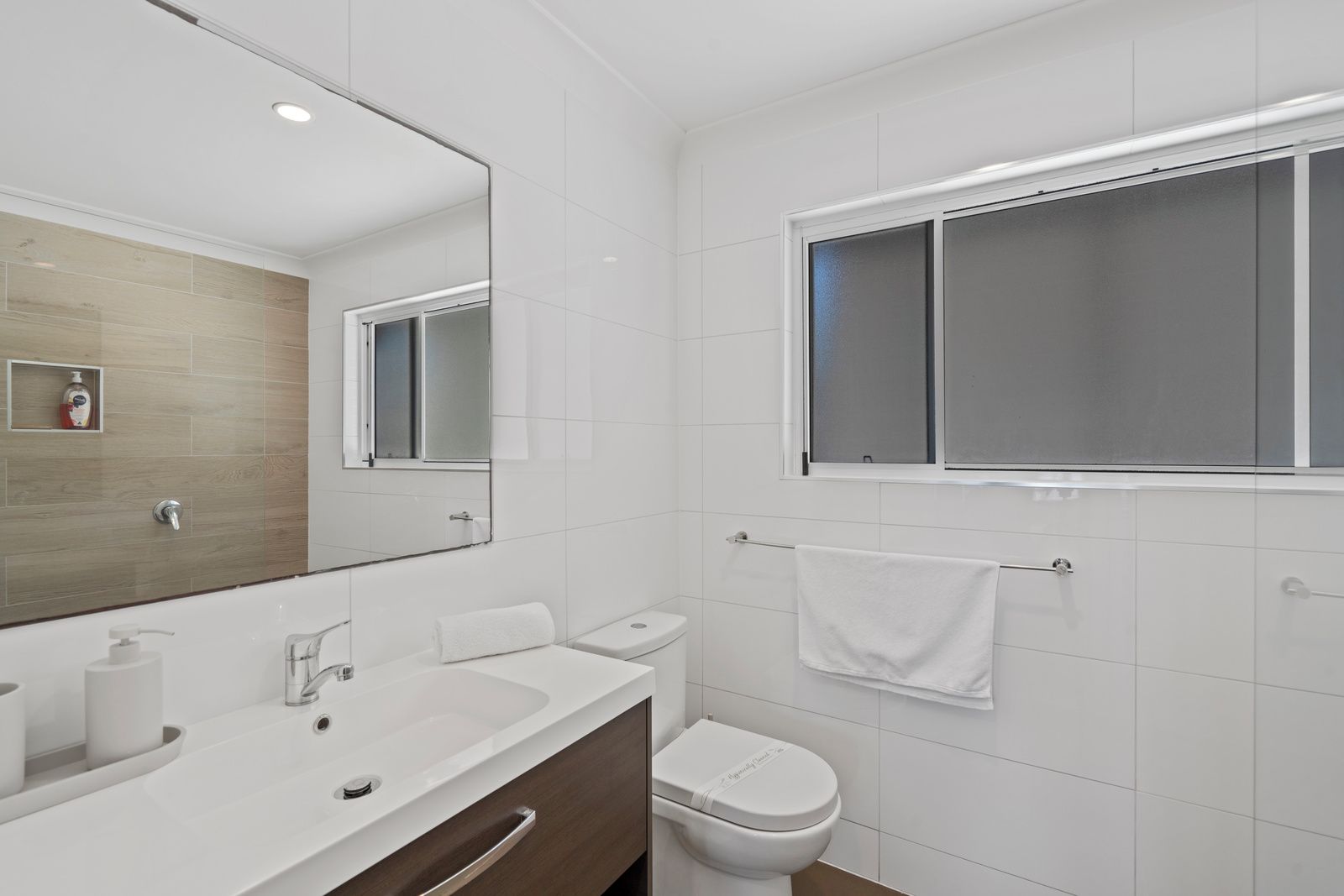 Un baño moderno con lavamanos, espejo e inodoro blancos.